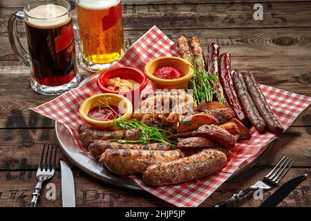 Delicious set of various fried sausages served with country style potato wedges, stewed cabbage and sauces garnished with fresh greens served as beer Stock Photo
