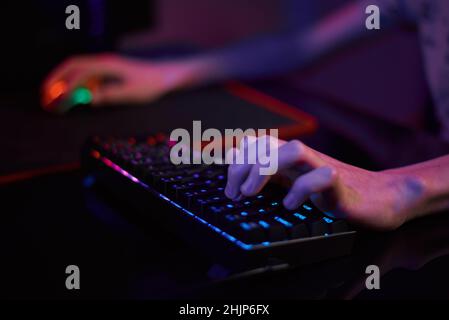 Professional gamer play computer video game in dark room, use neon colored rgb mechanical keyboard, place for cybersport gaming Stock Photo