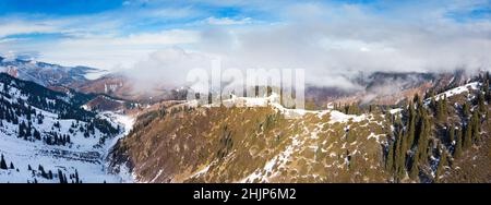 Winter in the mountains. The mountains cover the clouds. The slopes are covered with coniferous trees Stock Photo