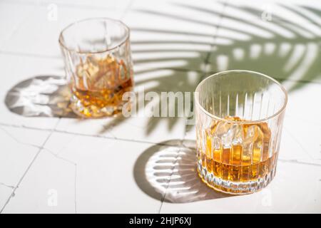 Whiskey with ice in glasses, white background with hard light, shadows and sun glare, copy space Stock Photo