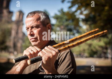 Escrima and kapap instructor demonstrates sticks fighting techniques in public park. Filipino Martial Arts. Eskrima. Kali. Stock Photo