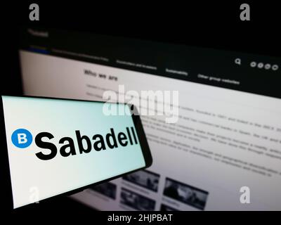 Mobile phone with logo of Spanish banking company Banco de Sabadell S.A. on screen in front of business website. Focus on left of phone display. Stock Photo