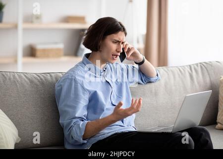 Displeased customer calling to hotline service. Discontented guy talking on cellphone using laptop, having problem Stock Photo