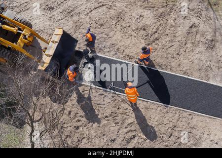 New road construction workers laying asphalt surface on walkway. Hot asphalt paving road workers team. Ground work. Groundwork. Ground construction Stock Photo