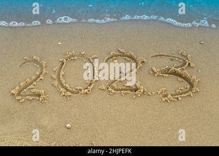 The numbers 2023 are written on the sand on the beach. The concept of