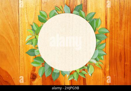 Green leaves and round paper card on wood texture. Horizontal banner with eco paper texture. Wooden planks, recycled carton material label and green l Stock Photo