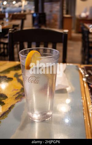 A glass of water in a clear drinking glass with the words CocaCola on it sits on a table in restaurant, shallow depth of field. Stock Photo
