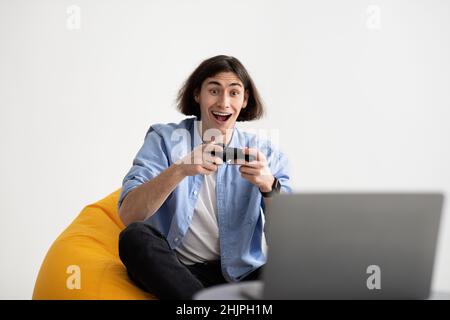 Gaming concept. Overjoyed man playing video game with joystick at home, sitting in beanbag chair, copy space Stock Photo