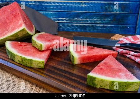 Triangular pieces of a delicious red watermelon on a wooden board. Healthy food, seasonal fruits. Chopped view. Stock Photo
