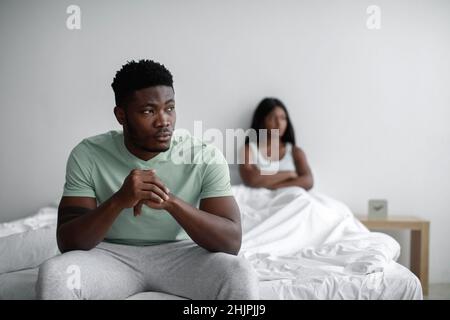 Depressed sad young black man ignores offended lady after quarrel sits on bed in bedroom interior, copy space Stock Photo