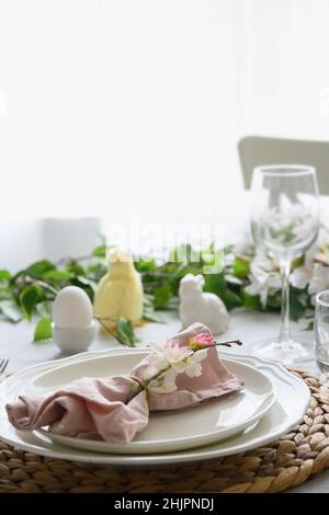 Easter table setting with yellow chick, festive decorations, fresh flowers and eggs. Elegance dinner at home interior. Close up. Stock Photo