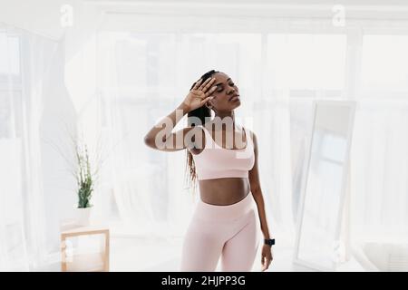 Millennial black woman resting after working out, feeling tired, wiping her forehead at home. Healthy lifestyle concept Stock Photo
