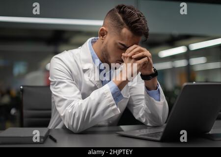 Exhausted middle eastern scientist sitting in front of laptop Stock Photo