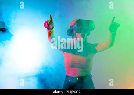Young woman using virtual reality glasses in the dark room with neon lighting. Wireless technologies. Stock Photo