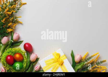 Easter composition. Multi-colored pearl eggs in a nest of tulip flowers a box with a gift on a gray background. Flat lay copy space top view border. Stock Photo