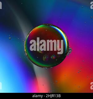 close-up of a dark oil drop on a color-lit water surface Stock Photo