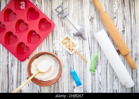 Preparing for baking: heart-shaped silicone mold, rolling pin, confectionery syringe, glaze, flour, sugar. Valentine's day concept. Top view. High quality photo Stock Photo