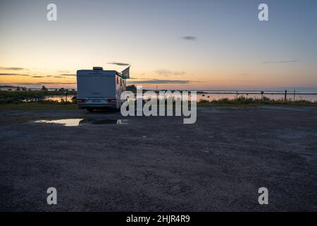 June 26, 2021 - Borgholm, Sweden: A camper van parked at an ocean bay in Boda in beautiful sunset light Stock Photo