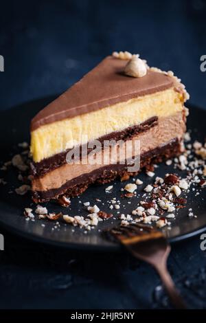 Nougat vanilla and chocolate glazed cake in four layers with hazelnuts on top and hazelnut crumbs around on a dark background Stock Photo