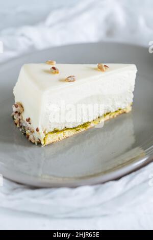 Four layer cake with pistachio, vanilla and white chocolate on grey plate with pistachios on top Stock Photo