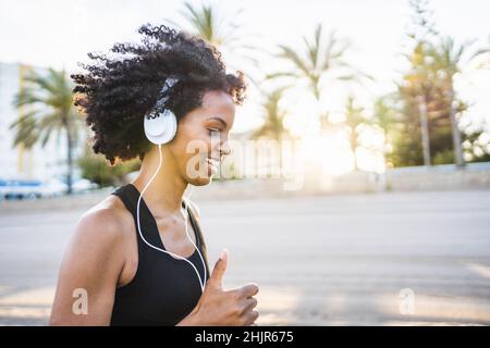 black woman with afro hair runs listening to music on the beach Stock Photo