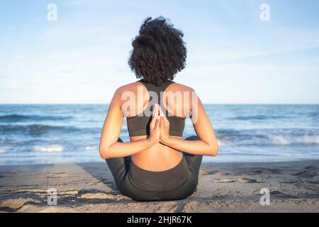 back of black woman sitting on the beach practicing yoga Stock Photo