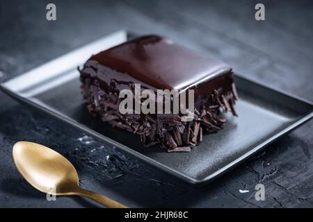 Glazed chocolate cake, one piece, on a dark black background on black plate with golden spoon Stock Photo