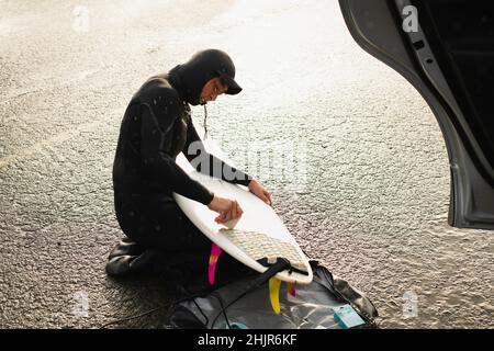 Young woman preparing to surf waxing surfboard in coastal Oregon Stock Photo