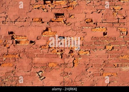Flaking red paint on a brick wall with many corroded and crumbling bricks Stock Photo