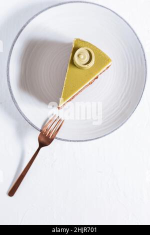 Pistachio chocolate cake with four layers and green pistachio glazing on top served on a white plate on white background with coffee in blur Stock Photo