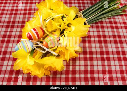 Festive Easter card. Easter bouquet of yellow daffodils and hand-painted eggs on a table with a checkered tablecloth. Place for your text. Spring bouq Stock Photo
