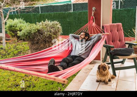relaxed man lying in a hammock enjoying at home with dog Stock Photo
