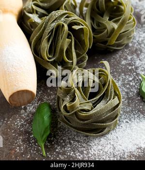 Tagliatelle Paglia e Fieno. on a dark background. Making homemade pasta linguine on rustic kitchen table with flour, rolling pin and pasta. Selective Stock Photo