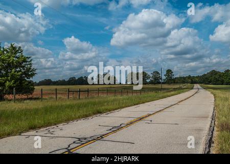 Rural backroad through the countryside with rustic fencing surrounding the farmland and tall grasses growing along the worn country road in Georgia on Stock Photo