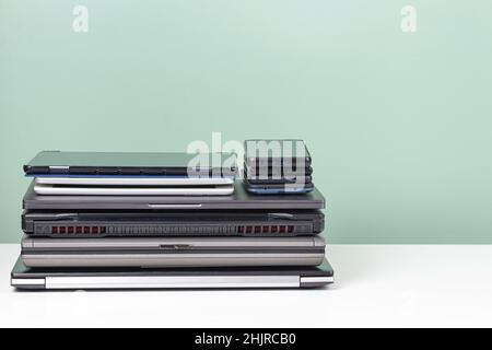 Pile of old used laptop computers, digital tablets, smartphones for recycling on white table. Planned obsolescence, e-waste, electronic waste for Stock Photo