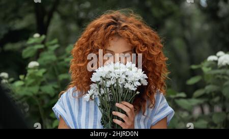 curly redhead woman with closed eyes smelling white flowers Stock Photo