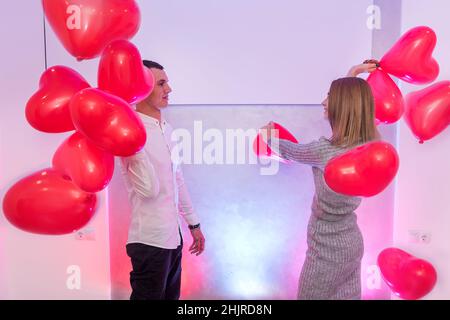 Beautiful couple with red air balloons celebrating Valentine's Day posing in studio Stock Photo