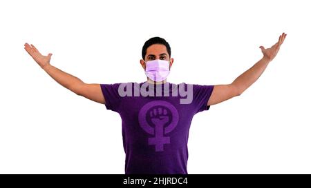 Portrait of feminist caucasian man wearing a purple shirt with strong fist raised up for woman gender and a medical mask during coronavirus outbreak. Stock Photo