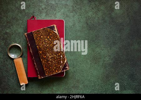 Magnifying glass with leather handle and old books on textured green background, top view Stock Photo