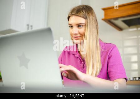 Online student typing on laptop computer at home on lockdown. Young blonde woman working on notebook pc. Freelancer female doing distant work with fas Stock Photo