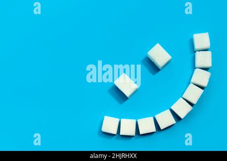 Sugar cubes are laid out on a blue background in the shape of a smile. Refined sugar Stock Photo