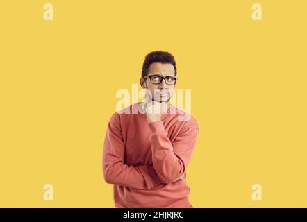 Puzzled male student in glasses isolated on yellow background thinking about something Stock Photo