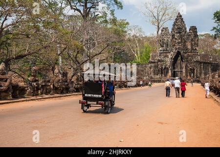 Siem Reap, Cambodia - February, 2013: Tourists on auto rickshaws and on foot visit the temple complex of Angkor Thom through the South Gate Stock Photo