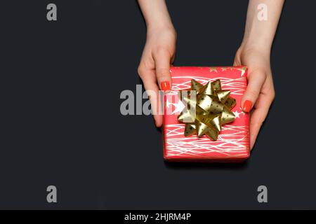 Beautiful red gift box with yellow bow in women's hands on a black background, copy space for text. Stock Photo