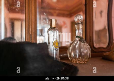 Italy, January 20, 2021. Woman's hat and antique perfume bottle on a piece of furniture in an abandoned house. urbex Stock Photo