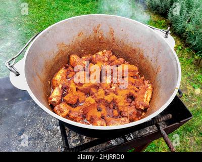 Delicious hungarian goulash in a kettle made outdoor at campfire. Beef meat marinated in adjika is stewed in a cauldron with tomatoes, bell peppers, p Stock Photo