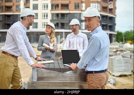 Builder standing among his three colleagues on the building site Stock Photo