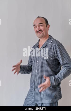 Dancing and singing happy senior Asian man in pajamas at home against gray wall . Stock Photo