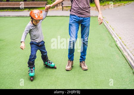 Dad teaches son to rollerblade in the park Stock Photo