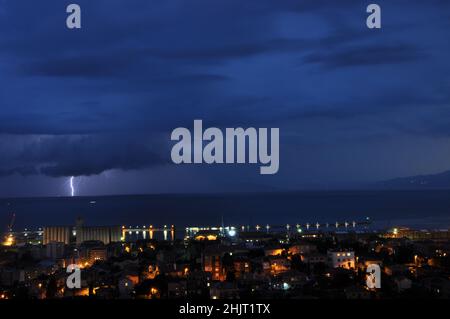 Stormy black clouds in Croatian coastline.Dark sky and black clouds at night, thunder bolt strikes Adriatic Sea. Rijeka city during thunder storm. Stock Photo